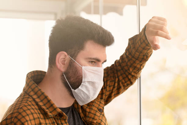 istock Man wearing a protective medical mask looking out of the window during quarantine 1215935518