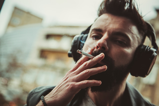 A young hipster man walks down the street with headphones on