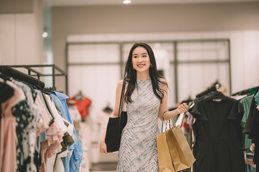 an asian chinese female shopping at clothing store for her clothes with shopping bags