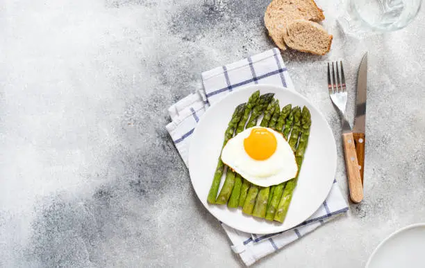 Organic healthy Asparagus and fried egg served on a white plate. Healthy vegetarian breakfast. Grey background. Copy space. Flat lay