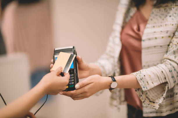 レジ係の衣料品店から服を買うアジアの中国人女性が、店員からのクレジットカードリーダーを通じて支払いのために彼女のクレジットカードを引き渡す - credit card reader ストックフォトと画像