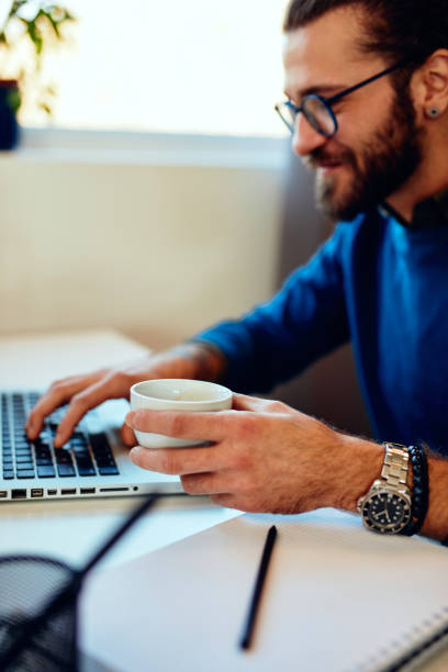 istock Young handsome bearded hipster sitting at his home office looking at his notebook. Work from home concept. 1215944993