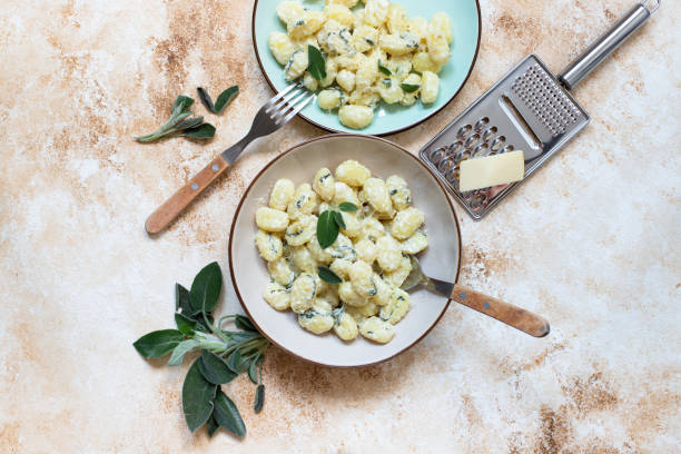 gnocchi fatti in casa italiani con burro, formaggio e salvia serviti in due piatti su un tavolo di marmo leggero. cibo italiano. copiare lo spazio. laici piatti - sugo pronto foto e immagini stock