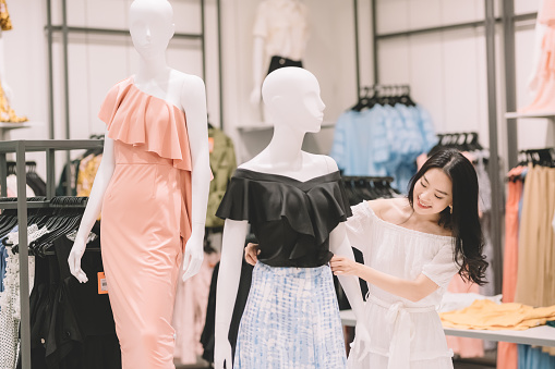 an asian chinese young woman sales assistant in shop adjusting and wearing for the mannequin in her clothing store