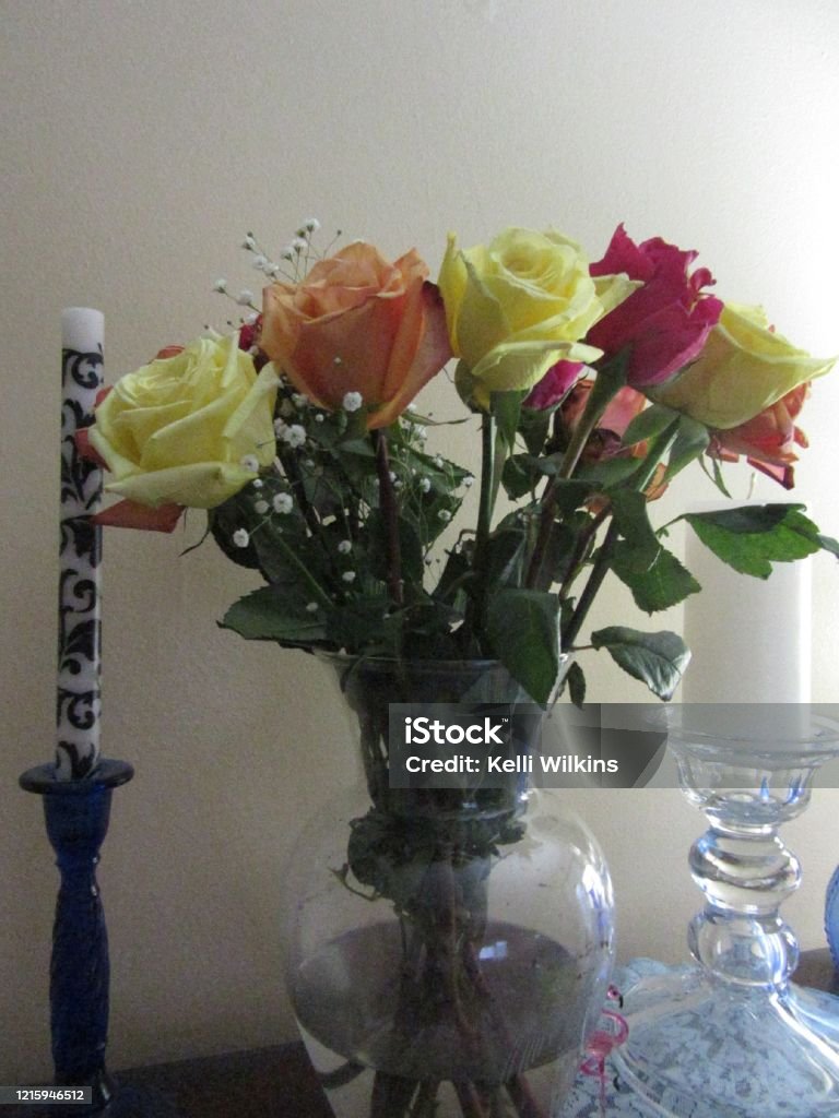Colorful Roses in Vase Next to Candle Yellow, orange and red blooming roses on display in a vase. Anniversary Stock Photo