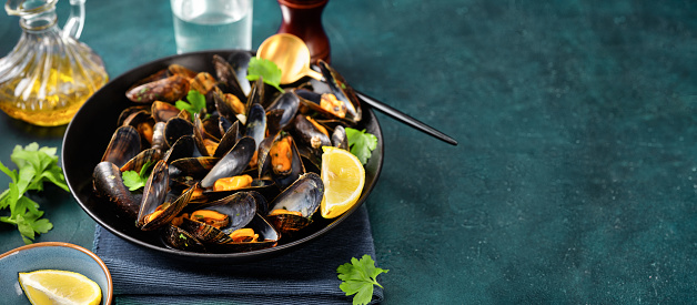 Delicious reshly cooked mussles in a plate with ingredients on dark turquoise background. Copy space