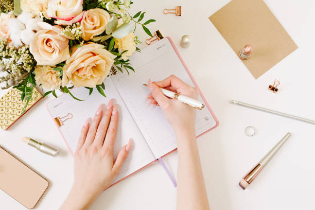 istock Female hands wtite in pink opened notebook on white background. Tender mood and blogging concept with beautiful roses bouquet and accesoires in flat lay style 1215953791