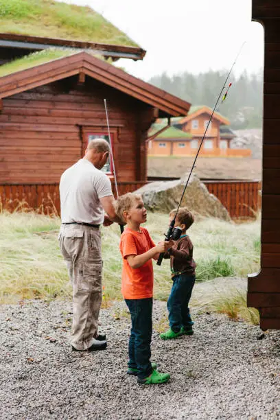 July 7, 2012 - Norway: two handsome little boys are getting ready to fish with their grandfather - holding fishing rods, being concentrated.