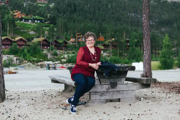 July 6, 2012 - Norway: pretty mature woman sitting on a bench at gorgeous nature surroundings in Norway, wearing red blouse, eyeglasses, smiling cheerfully, being happy and relaxed