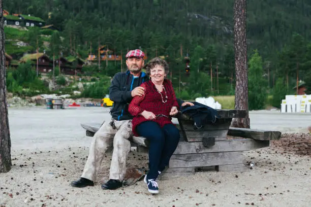 July 6, 2012 - Norway: handsome mature couple - man and wife - togetherness and bonding, long lasting love and relationship. They are sitting together, embracing, in a beautiful background in Norway in summer