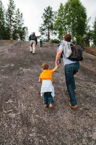 June 28, 2013 - Norway: two boys, brothers, their dad and grandad are climbing a rock, rear view, father holding hands with a toddler.