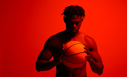Red filtered shot of a young sportsman posing with a basketball in the studio