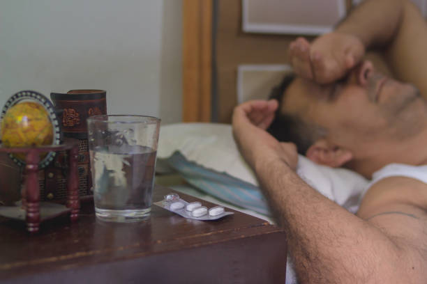 istock sick man lying down and holding pills at light table 1215962341