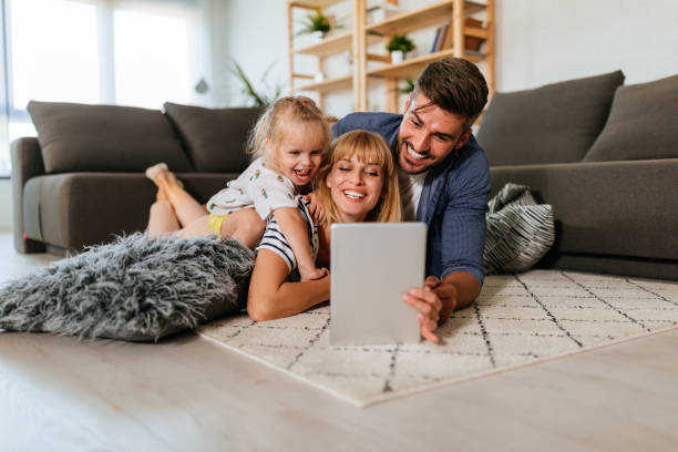Share the love, share the fun Young female using a digital tablet with her daughter and husband while lying on the floor at home family at home stock pictures, royalty-free photos & images