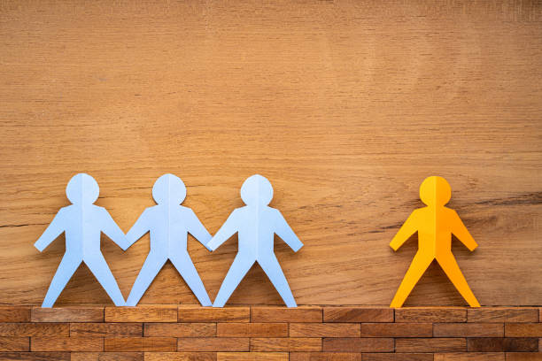 istock Paper cutout human figures separate by wide space between them on wood background, social distancing concept during COVID-19 virus outbreak 1215969314