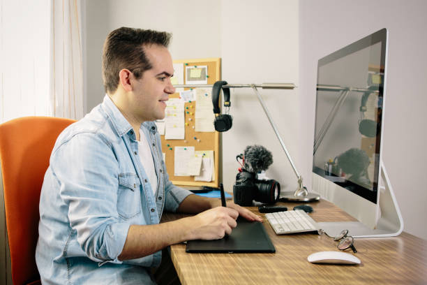 istock Boy photographer working from home on his computer. On the table are an electronic graphics tablet and a photo camera 1215983364