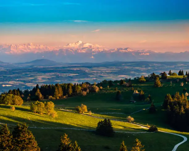 View over the country and the green valleys to the Alps on the horizon. viewpoint near the Solitat summit at an altitude of 1400 meters in the Jura from Neuchâtel, Lake Neuchâtel, Canton Neuchâtel to Canton Vaud, Switzerland.