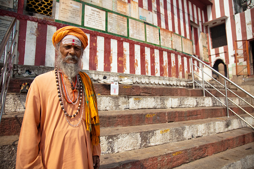 Varanasi - Ottobre 31,2016:  A long-bearded sadhu, or holy man sitting on the streets of Varanasi. This is one of the oldest inhabited cities in the world and also the holiest of the seven sacred cities in Hinduism and Jainism and so the most important pilgrimage place for hindus. Many ascetics in Varanasi like the one in the picture stay in visible places in the ghats decorated with images of the hindu gods to attract the attention and donations of pilgrims and tourists.