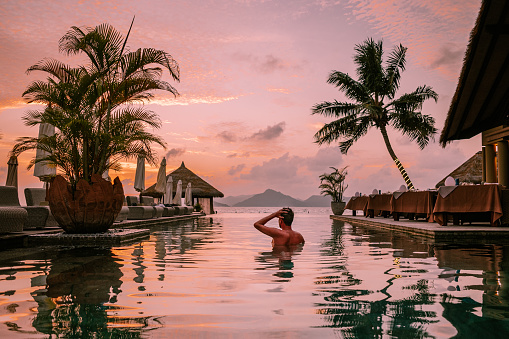 young men in swimming pool during sunset, Luxury swimming pool in tropical resort, relaxing holidays in Seychelles islands. La Digue, Young guy during sunset by swimpool