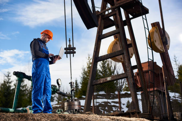 istock Oil engineer with a laptop standing next to an oil rig making notes in his computer 1215993717
