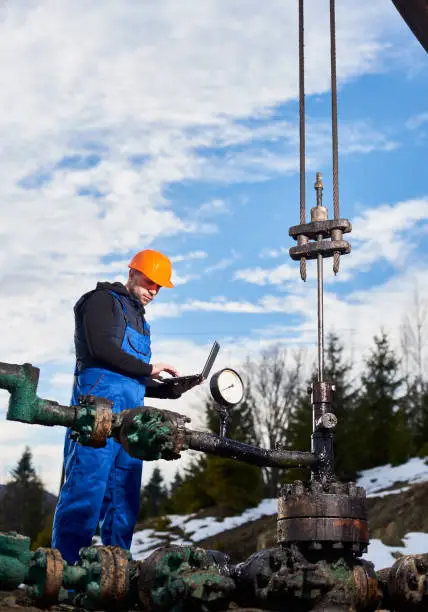 Photo of Petroleum engineer using laptop in oil field.