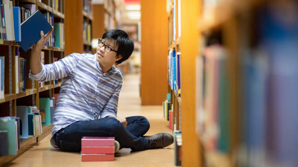 istock Smart Asian man student reading book in library 1215996669
