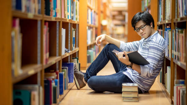 Smart Asian man student reading book in library Smart Asian man university student wearing glasses reading book by vintage bookshelf. Textbook resources in college library for educational subject and research. Scholarship for education opportunity. philosophy stock pictures, royalty-free photos & images