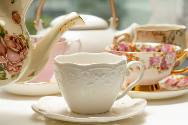 Hot tea cup with spoon on white plate, white kettle, cafe blurred on background, breakfast concept.