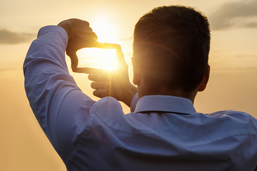 Businessman showing cropping composition gesture against the background of the sun.