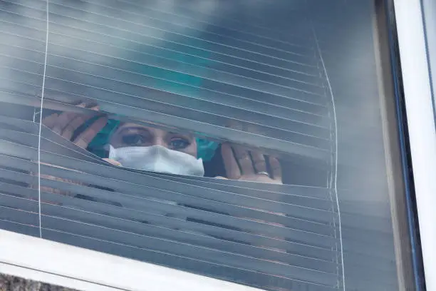 Woman with mouthguard looking through blinds