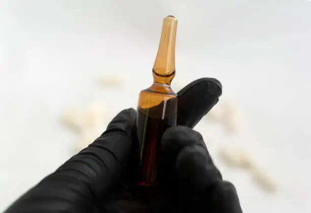 Photo of Hand in black latex glove holding medical glass ampule with medicine