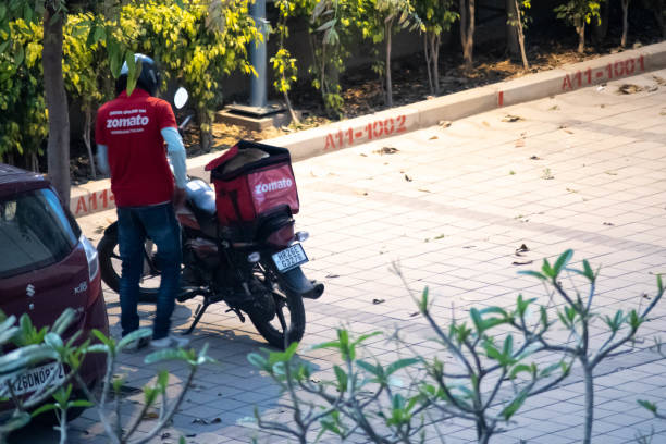 zomato corriere che indossa la camicia rossa in attesa vicino alla sua bici con la borsa di consegna zomato - image title foto e immagini stock