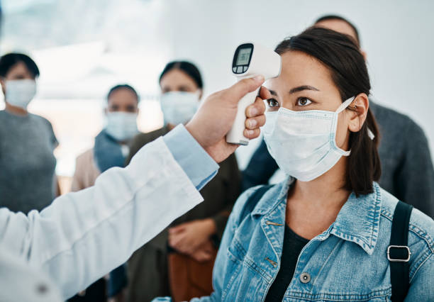 Will it be quarantine for you? Shot of a young woman getting her temperature taken with an infrared thermometer by a doctor during an outbreak prevention photos stock pictures, royalty-free photos & images