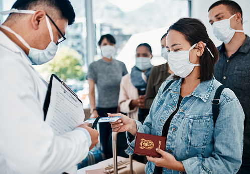 Shot of a woman wearing a mask and giving her passport to a doctor in an airport