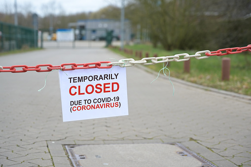 Barrera de cadena blanca roja y signo con texto Temporalmente Cerrado debido a Covid-19 Coronavirus, frente a una empresa borrosa, bloqueo pandémico en todo el país, espacio de copia, photo