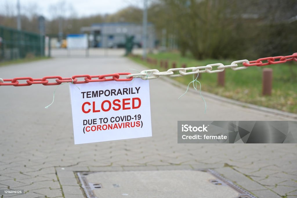 Red white chain barrier and sign with text Temporarily Closed due to Covid-19 Coronavirus, in front of a blurred company, countrywide pandemic lock down, copy space, Red white chain barrier and sign with text Temporarily Closed due to Covid-19 Coronavirus, in front of a blurred company, countrywide pandemic lock down, copy space, selected focus Lockdown Stock Photo