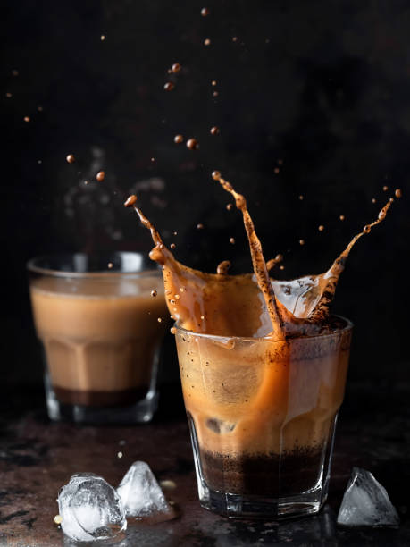 istock Splash in a glass with ice coffee on a dark background. Refreshing iced cappuccino drink with ice cubes. A wave of cold drink. Close up, vertical orientation, space for text. Shallow depth of field. 1216018126