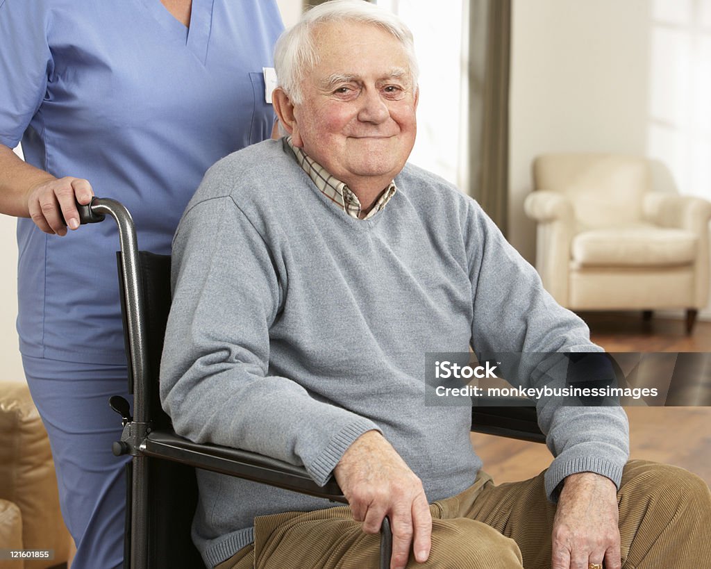Disabled Senior Man Sitting In Wheelchair With Carer  Home Caregiver Stock Photo