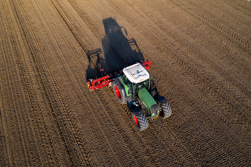 Tractor drilling seed in plowed field viewed from above.