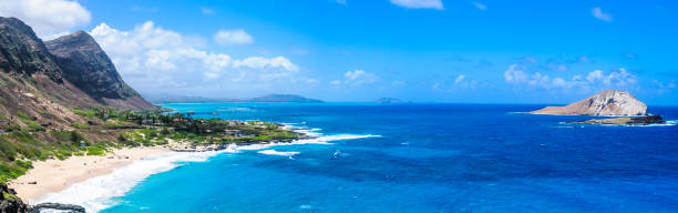 Steep volcanic mountains form a backdrop for Waimanalo Beach on the eastern shore of Oahu where swimmers and beach goers enjoy a large  uncrowded beach with soft sand and views of Rabbit Island.
