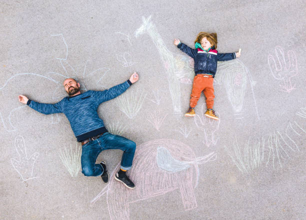 istock Young kid with his father drawing on the asphalt colored with chalk 1216031058