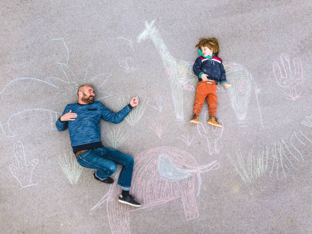 istock Young kid with his father drawing on the asphalt colored with chalk 1216031587