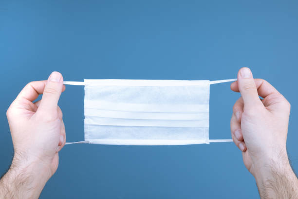 istock Hand holding white medical protective mask on blue background 1216035966
