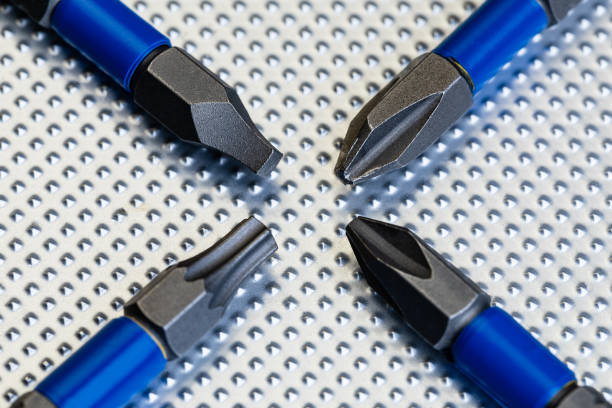 A macro image of 4 drill driver bits, 2 phillips head, a star driver and a square drive, on a steel industrial surface in an X pattern with room for copy all around the bits on the steel surface.