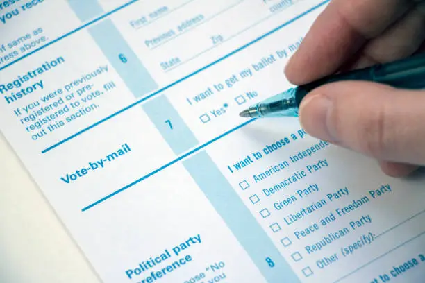 Closeup of Vote-by-Mail section of a voter registration form with hand holding a pen near the 'Yes' checkbox