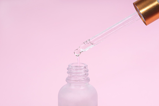 Dropper glass Bottle Mock-Up. Oily drop falls from cosmetic pipette on pink background. Skin care concept.