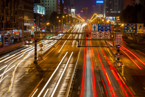 A night street scene with car light trails, residential and office buildings with advertisements, neon lights and billboards, COVID-19 epicenter, Hubei Province, China.