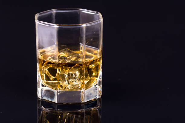 istock Octagon square glass with whiskey and ice cubes on the black background with reflections 1216044500