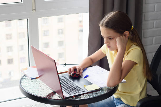 istock Girl thoughtfully doing homework, sitting at a table by the window 1216044948