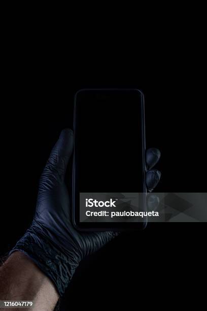 Hand Holding A Black Phone Isolated On A Black Background With A Black Gloves Stock Photo - Download Image Now